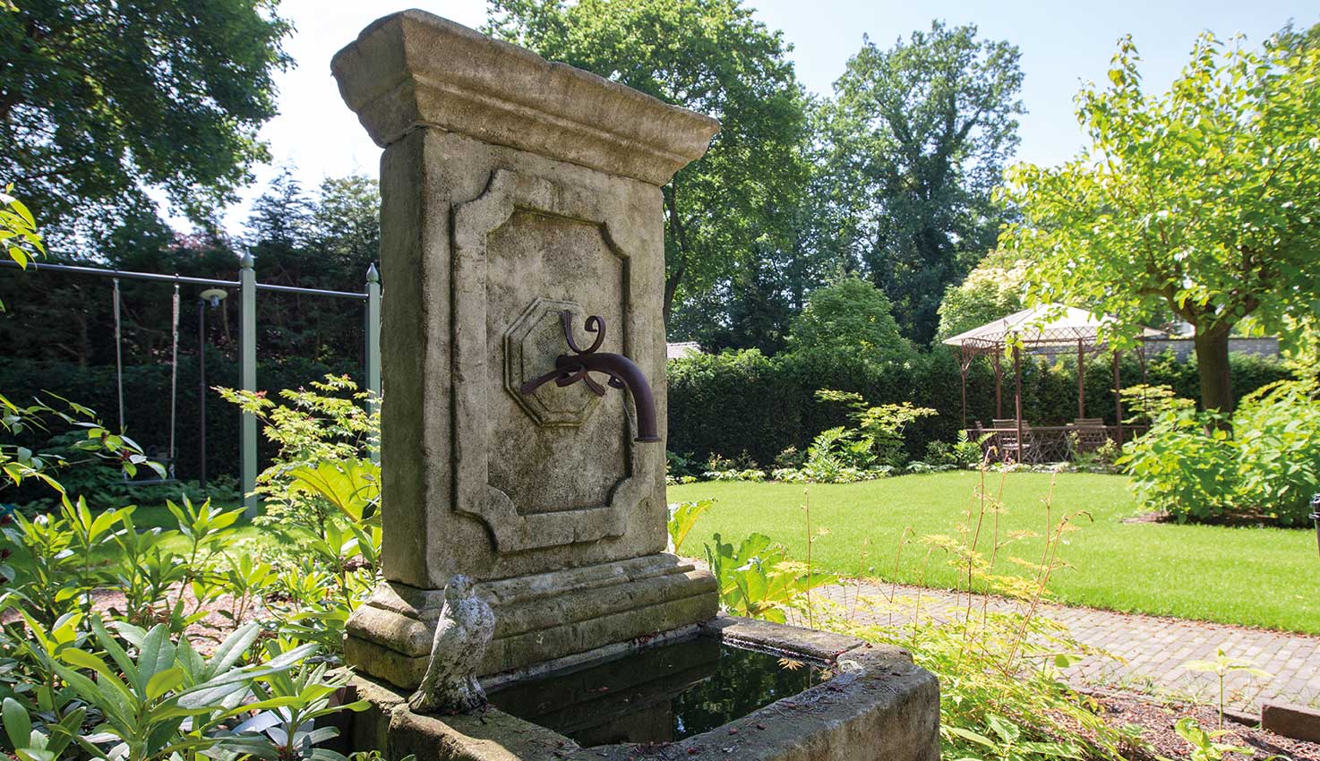 Klassieke tuin in Nunspeet met chique beplanting en blikvangers als een fontein, sierlijke lampen en antieke ornamenten rondom monumentale villa.